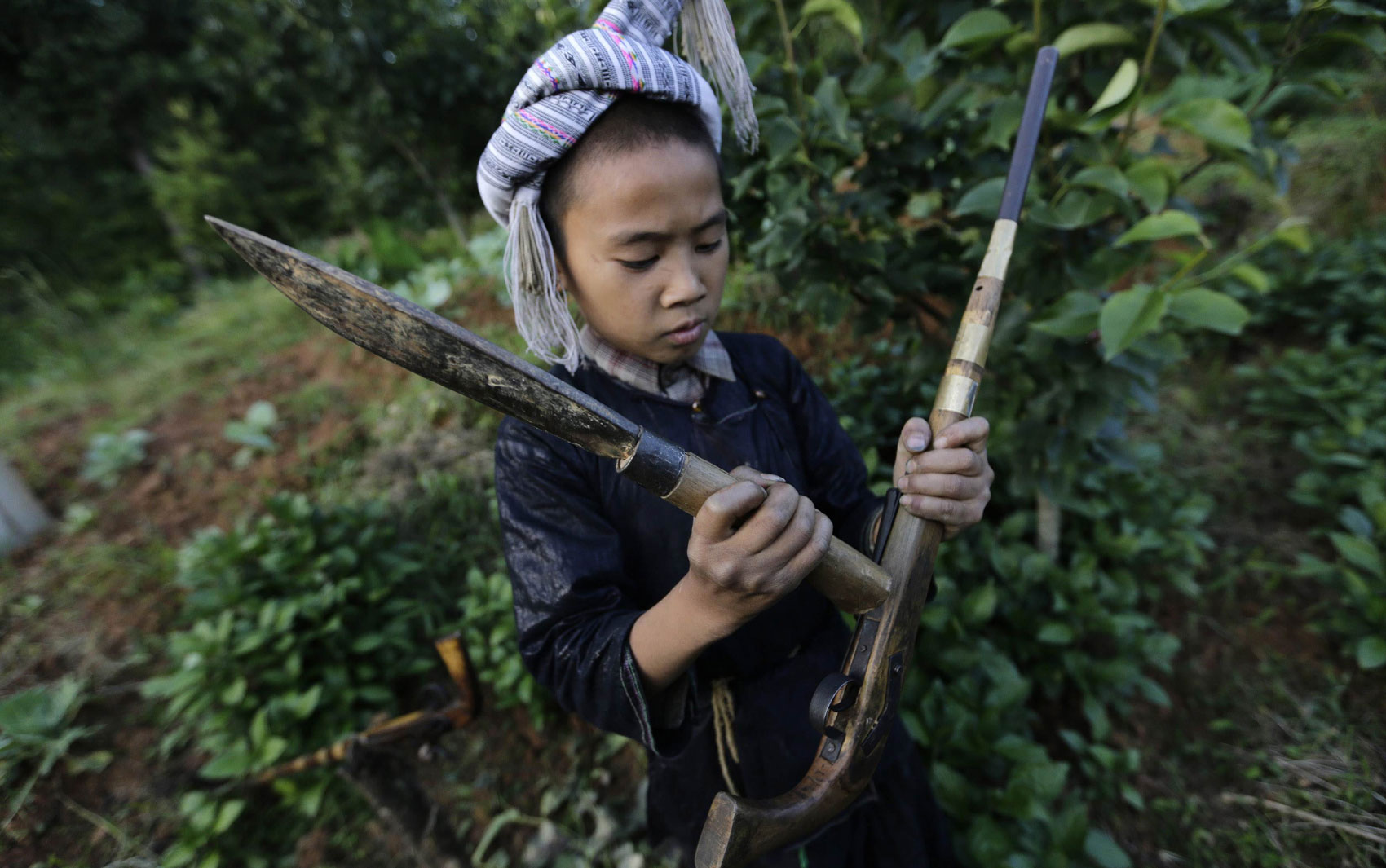 Gun Diuliang, de 10 anos, bate com o fundo de um facão contra sua arma para tampar o recipiente de pólvora antes de praticar tiros na vila de Basha.