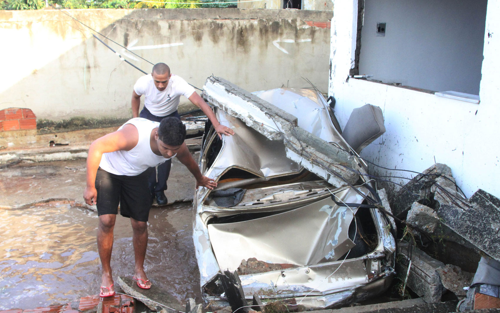 Homens passam por carro destruído pela água no bairro de Campo Grande, no Rio