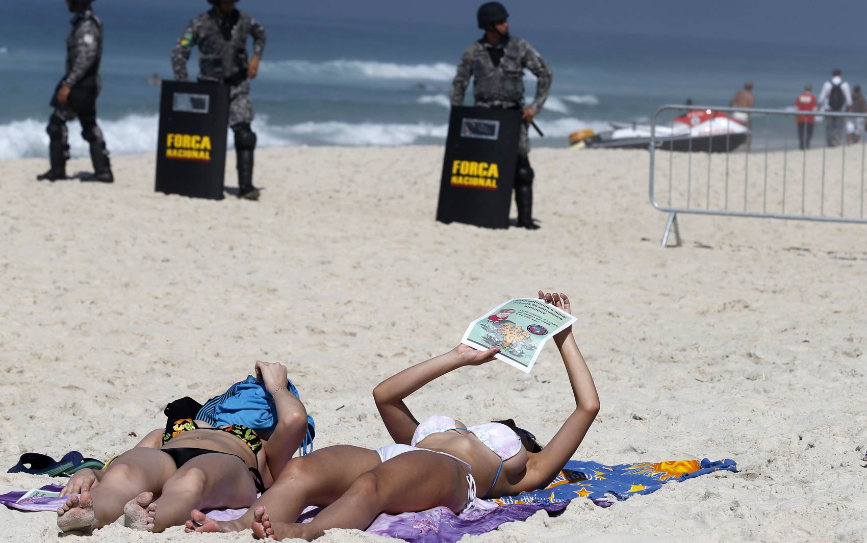 Banhistas tomam sol na praia da Barra da Tijuca, com militares da Força Nacional ao fundo
