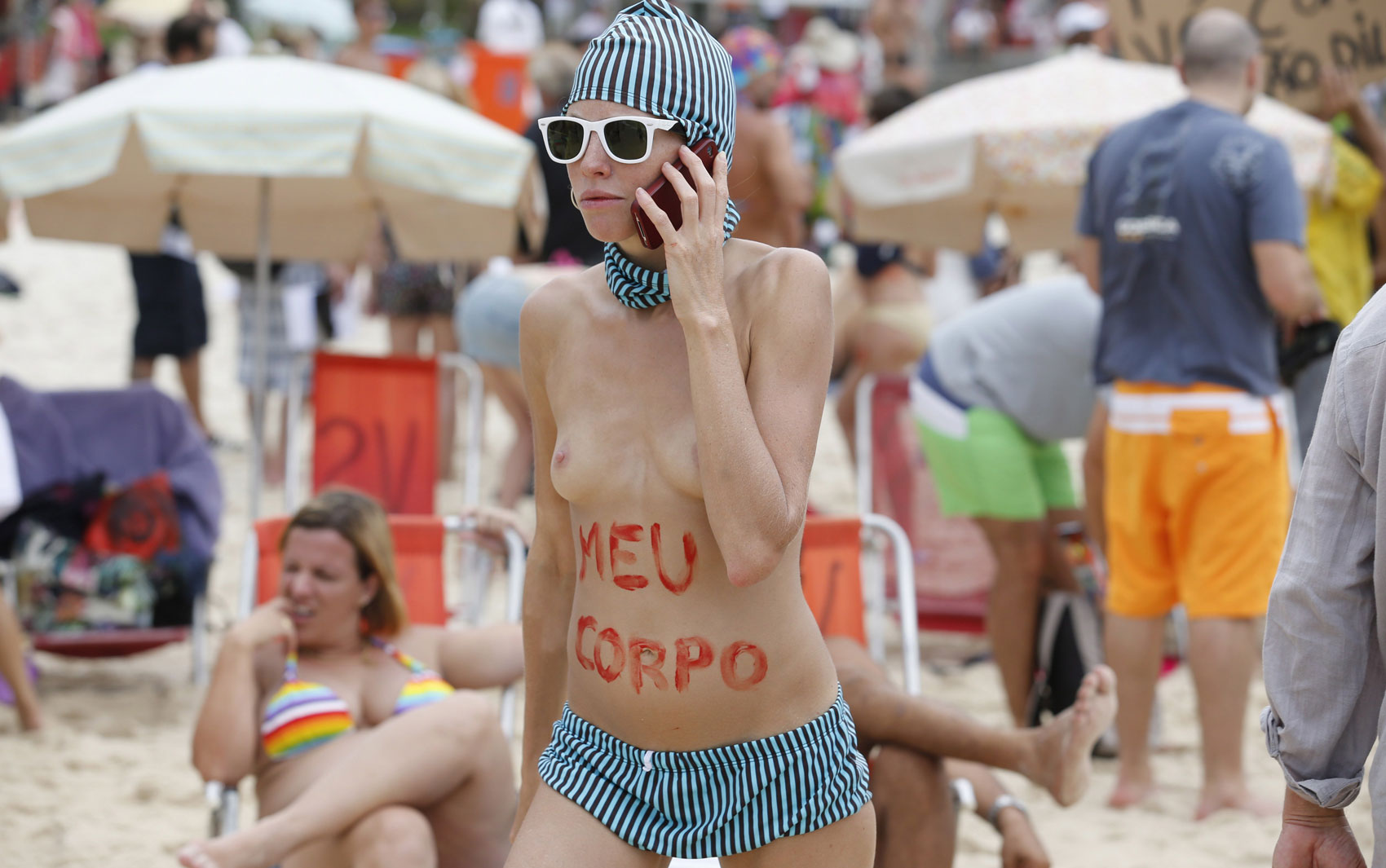 Manifestante fala ao celular após escrever as palavras "meu corpo" na barriga, na praia de Ipanema, no Rio