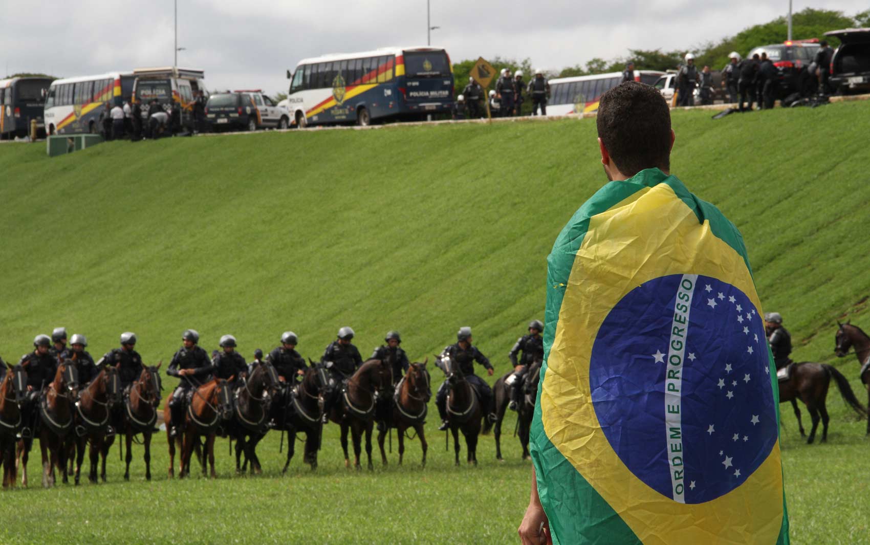 Enrolado na bandeira do Brasil, homem vê movimentação da polícia junto ao Congresso Nacional
