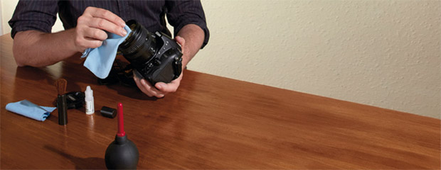 Kit de limpeza sobre mesa e fotógrafo limpando parte frontal da lente com lenço de microfibra (Foto: Reprodução/Digital Camera World)