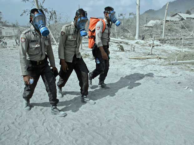 Policiais usam máscaras para investigar povoado atingido por nuvem de cinzas do vulcão Merapi em Kinahrejo, na Indonésia.
