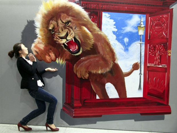 Mulher interage com pintura exposta em mostra de arte contemporânea na província chinesa de Jilin, no sábado (14), que mostra o salto de um leão. (Foto: AFP)