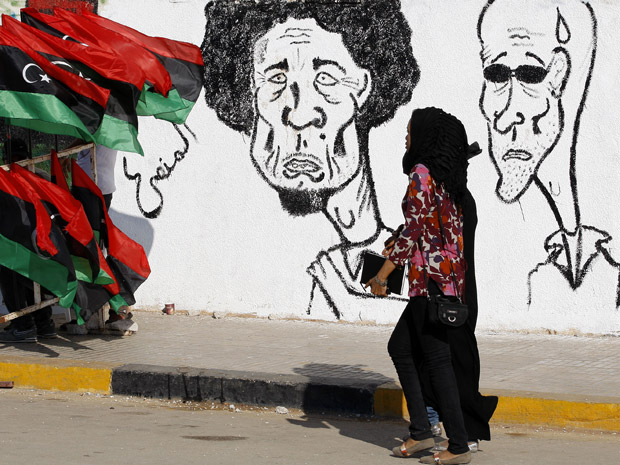 Mulher passa por caricatura de Kadhafi nesta quinta-feira (30) na cidade rebelde líbia de Benghazi (Foto: AP)