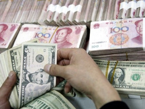 Chinês conta notas de dólar perto de notas de iuan. (Foto: AFP)