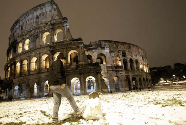 Garoto brinca com bola de neve em frente ao prédio do Coliseu, em Roma, após nevasca que 'branqueou' a capital da Itália na madrugada deste sábado (11) (Foto: AP)