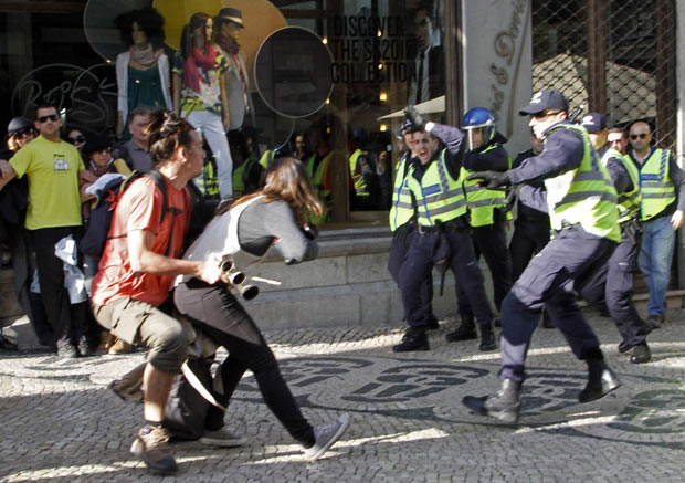 Um colega tenta retirar fotógrafa de local enquanto policias se aproximam, durante protestos  (Foto: Hugo Correia / Reuters)