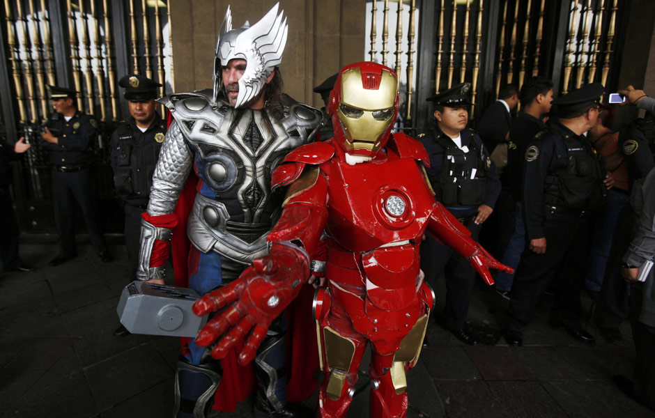 Artistas vestidos como Thor e Homem de Ferro posam para fotógrafos ao lado de uma linha de policiais durante uma manifestação em frente ao um prédio do governo mexicano, na Cidade do México, nesta sexta-feira (13).