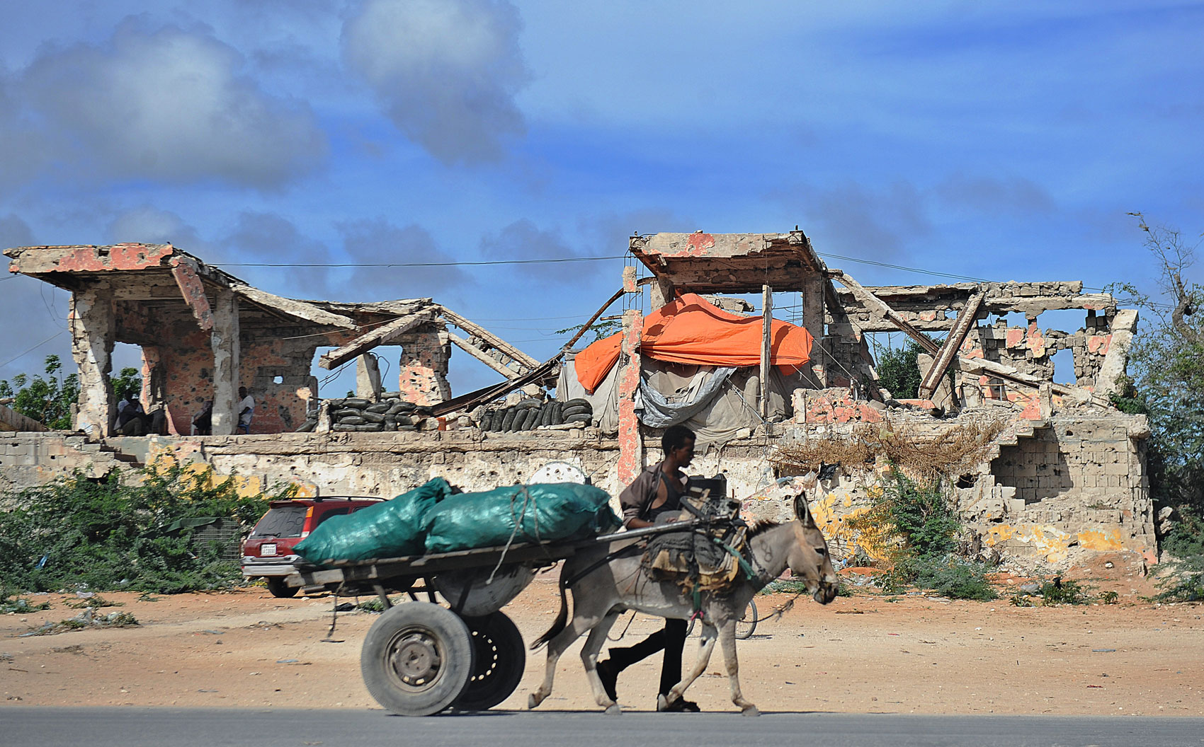 Homem caminha com animal e sacos de carvão perto de edifício atingido pela guerra na capital somali, em 23 de abril