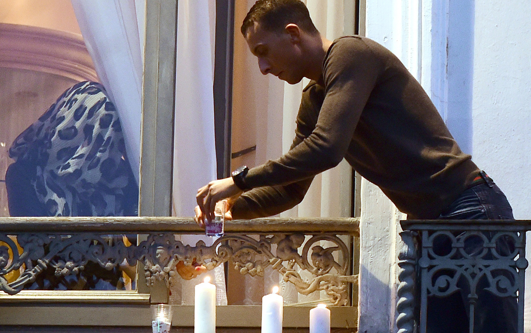 Mohamed Abdeslam, irmão de um dos homens que participou dos ataques terroristas em Paris, acende velas na sacada do apartamento de sua família durante uma vigília no distrito de Molenbeek, em Bruxelas, na quarta (18)
